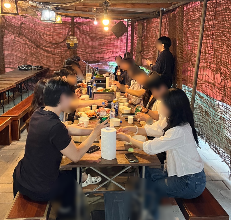 얼굴이 비식별 처리된 참가자들이 긴 테이블에서 대화하는 OVERSTAY 실제 운영 현장